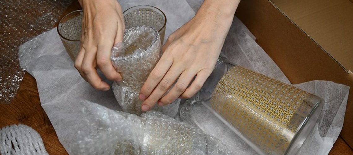 Hands pack up and wrap glassware into plastic bubble wrapping